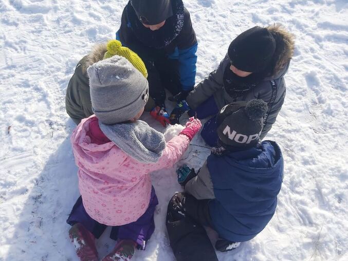 Dzieci siedzące w kręgu, bawiące się śniegiem